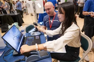 A CMU student uses a flight simulator, interacting with a laptop and gaming controls with a professional at a career fair