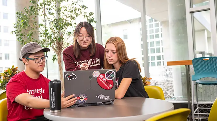 Three students look at a laptop together.